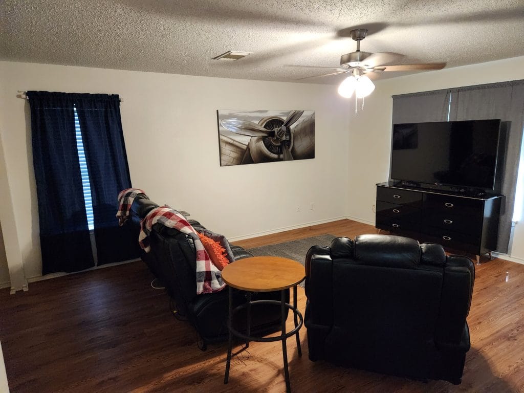 Spacious living area with modern furniture, large TV, ceiling fan, and polished wood floors for comfort and style | Dream TDY