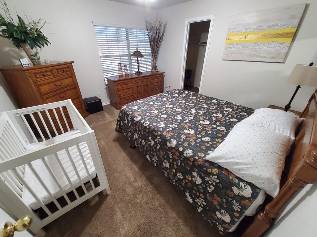 Cozy bedroom featuring a floral queen bed, crib, and ample storage. Clean, bright, and welcoming atmosphere | Dream TDY