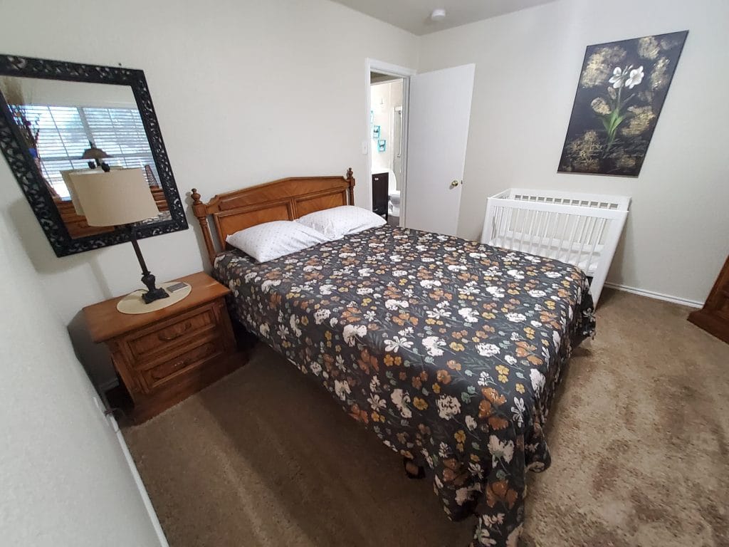 Cozy bedroom with floral bedding, a mirror, and a crib. Clean, inviting space ideal for relaxation and rest | Dream TDY