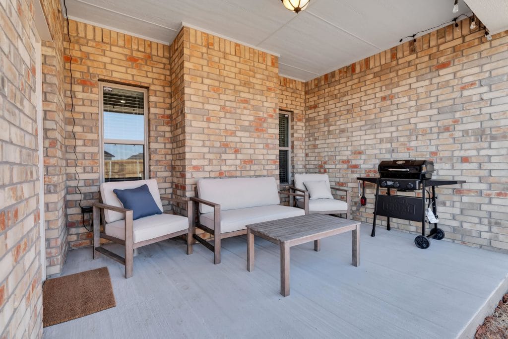 Relax on a cozy covered patio featuring stylish seating and a barbecue grill, perfect for outdoor gatherings and meals | Dream TDY 