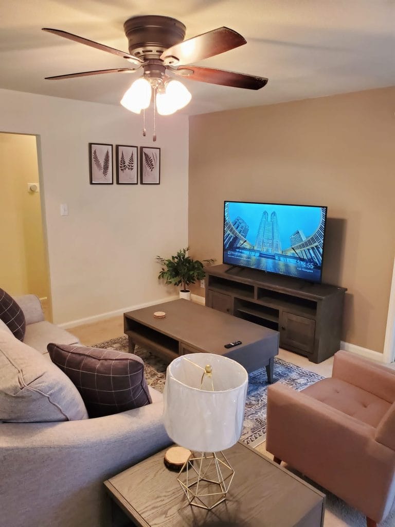 Cozy living area with modern furniture, ceiling fan, and large TV for relaxation. Perfect for short-term stays | Dream TDY