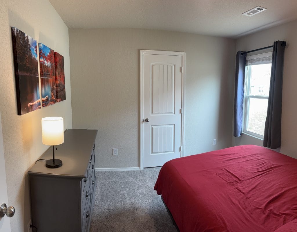 Cozy bedroom featuring a red bedspread, modern dresser, and ample natural light. Perfect for relaxation and comfort.