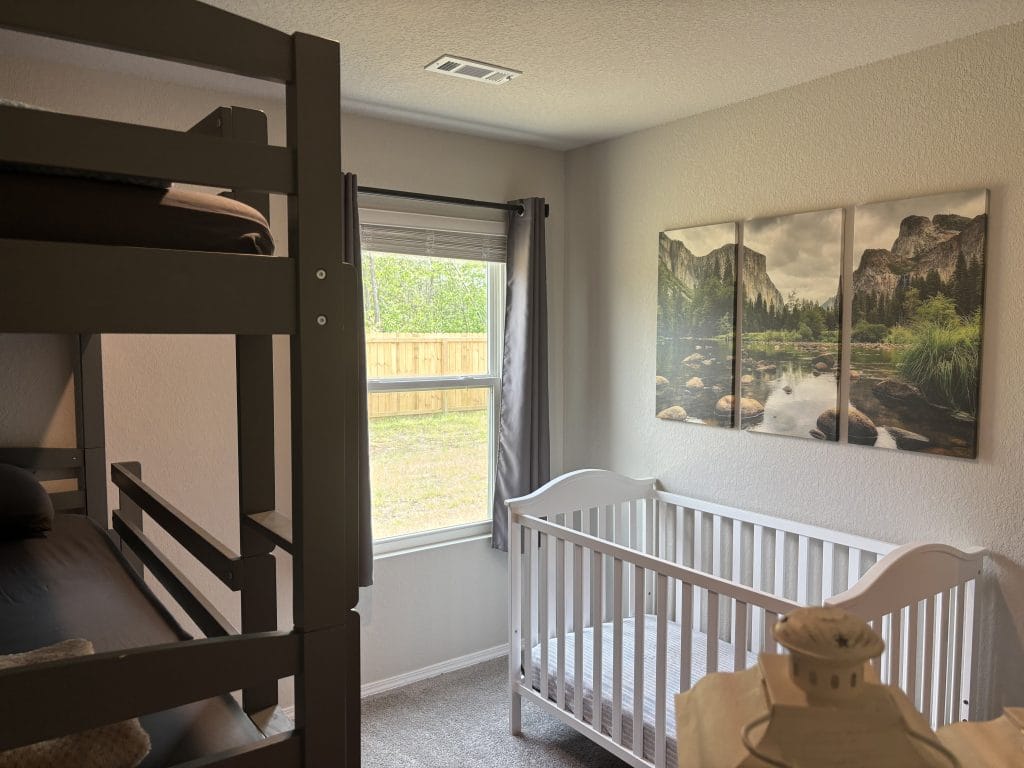 Cozy bedroom with a bunk bed and crib, featuring natural light and serene wall art. Perfect for families on short stays. | Dream TDY