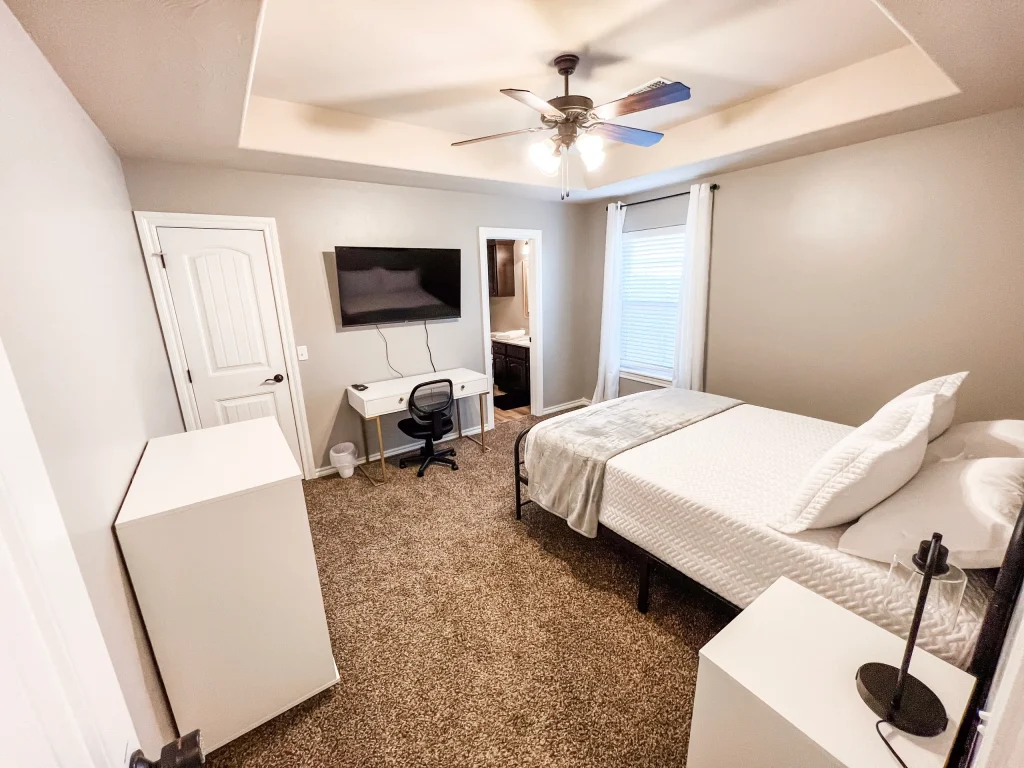 Cozy bedroom with modern decor, dedicated workspace, plush carpeting, and wall-mounted TV for comfort and productivity | Dream TDY