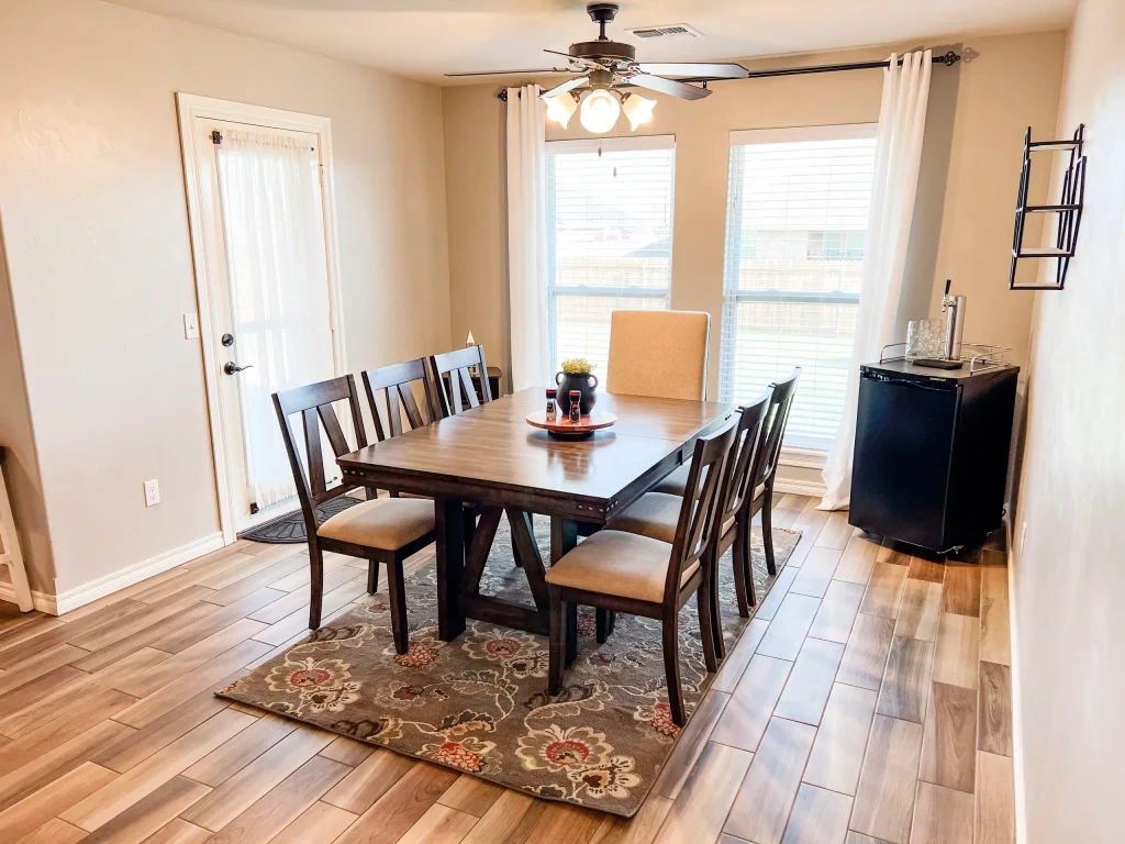 Bright dining area features a modern table, spacious seating, and adjacent mini-fridge, perfect for relaxed meals | Dream TDY