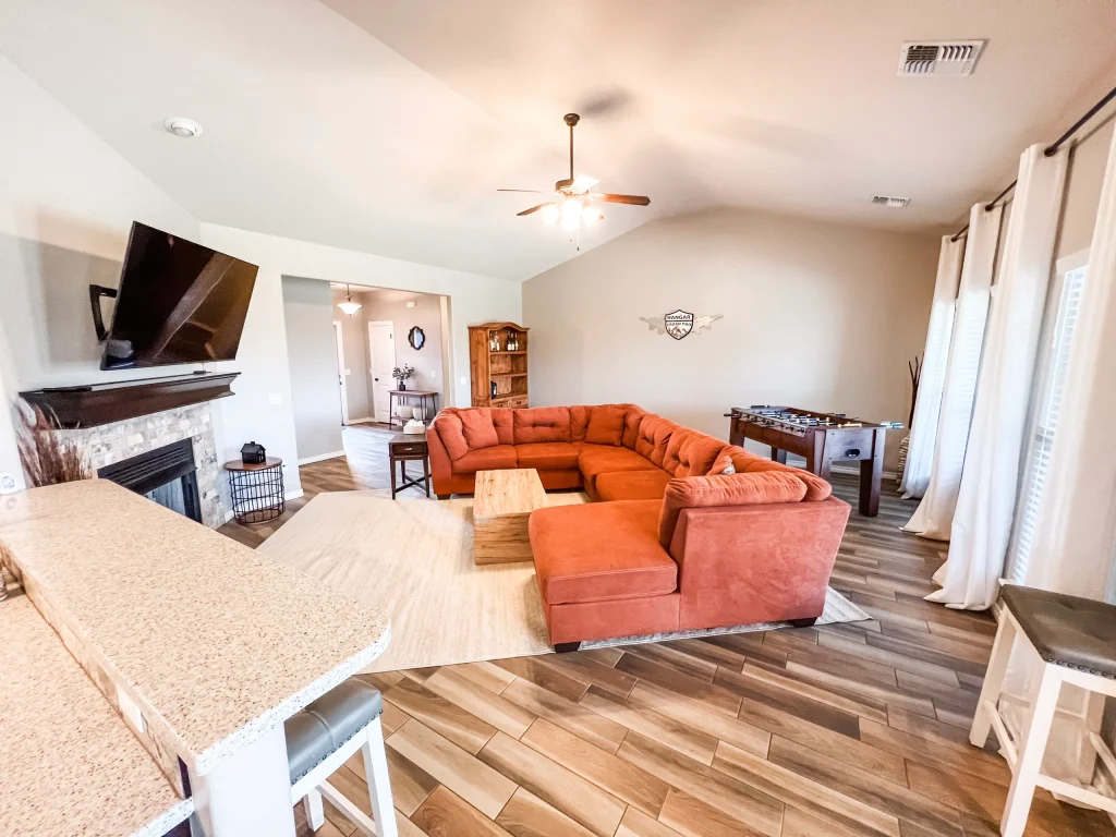 Spacious living area with cozy orange sectional, modern appliances, and a foosball table for relaxation | Dream TDY